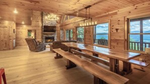 Interior de una cabaña de madera con chimenea, ventanas amplias y una zona de comedor.