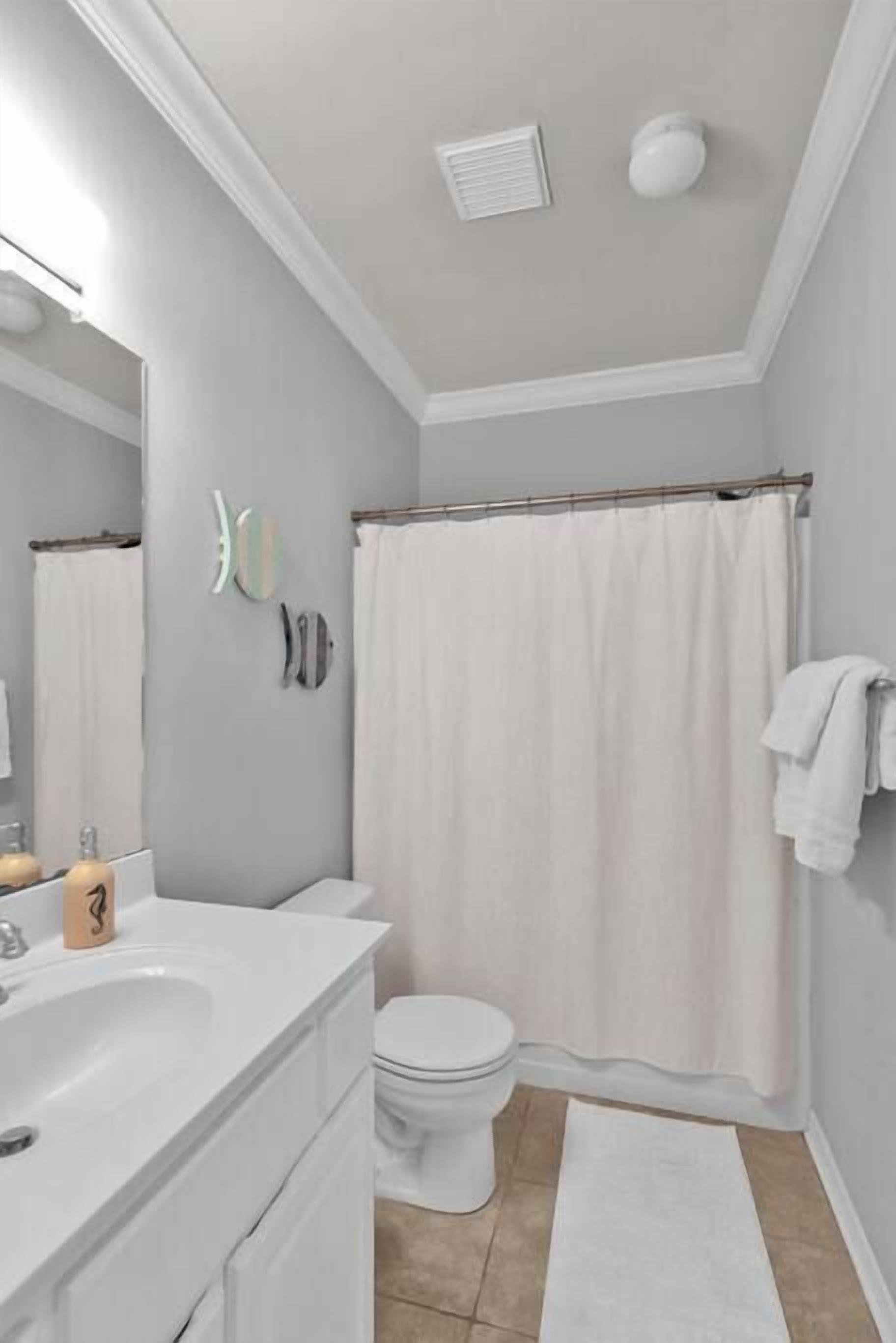 Un baño con un lavabo blanco, un espejo y un inodoro. Hay una cortina de ducha y un perchero con toallas.