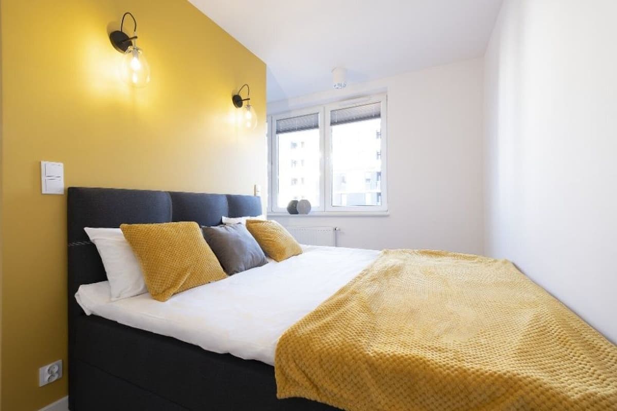 Un dormitorio con cama, paredes amarillas y una ventana.