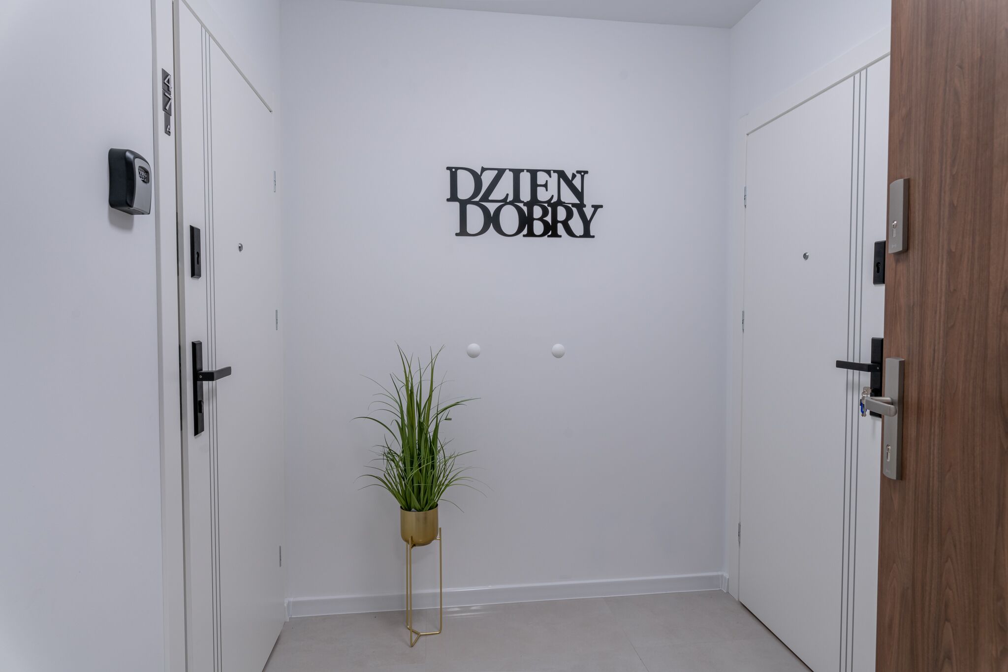 Un pasillo con paredes blancas, una planta en maceta y un letrero que dice 'DZJEN DOBRY'.
