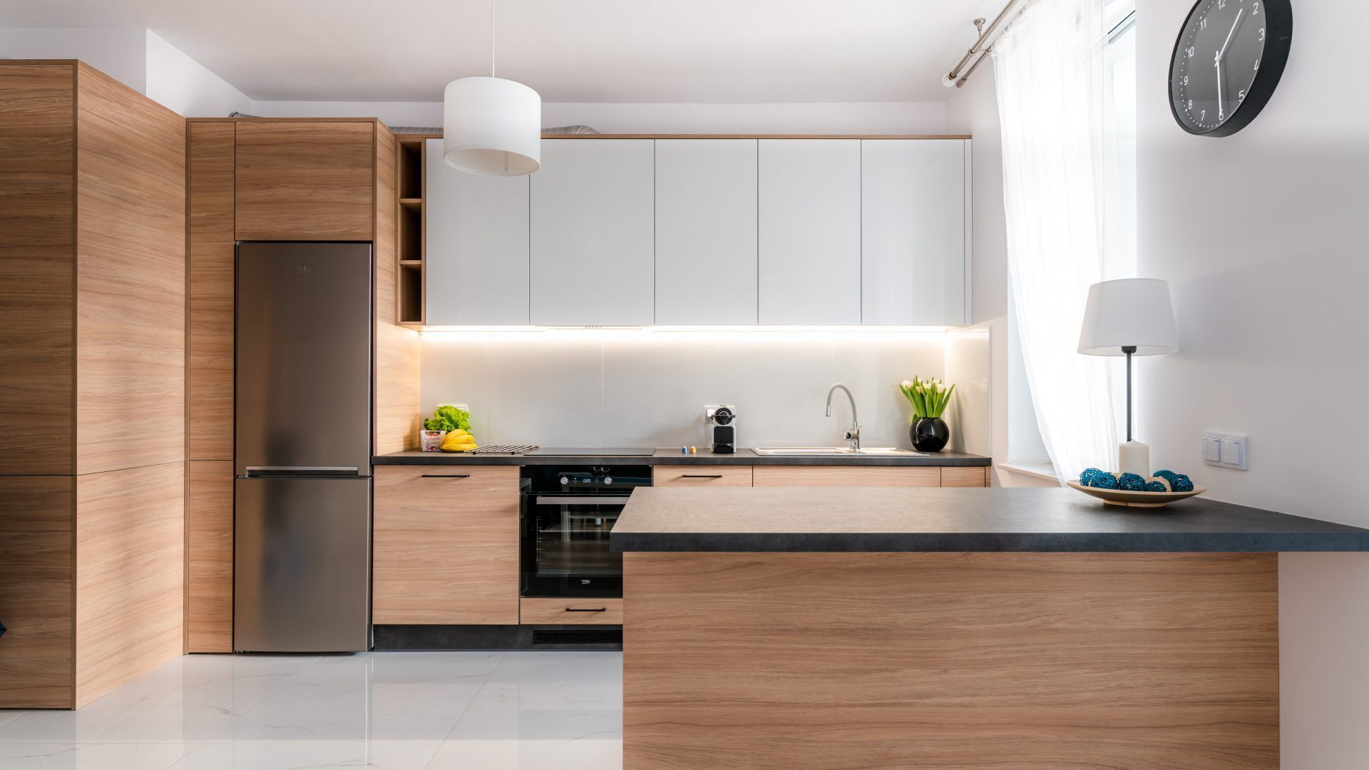 A modern kitchen with wooden cabinets, a stainless steel refrigerator, a built-in oven, and a black countertop.