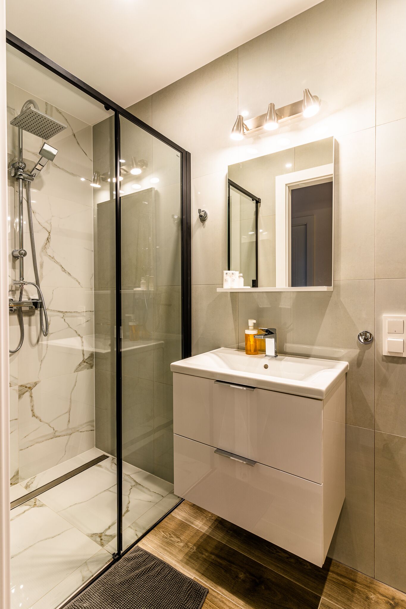 A modern bathroom with a glass-enclosed shower, a vanity with a mirror, and a wooden floor.