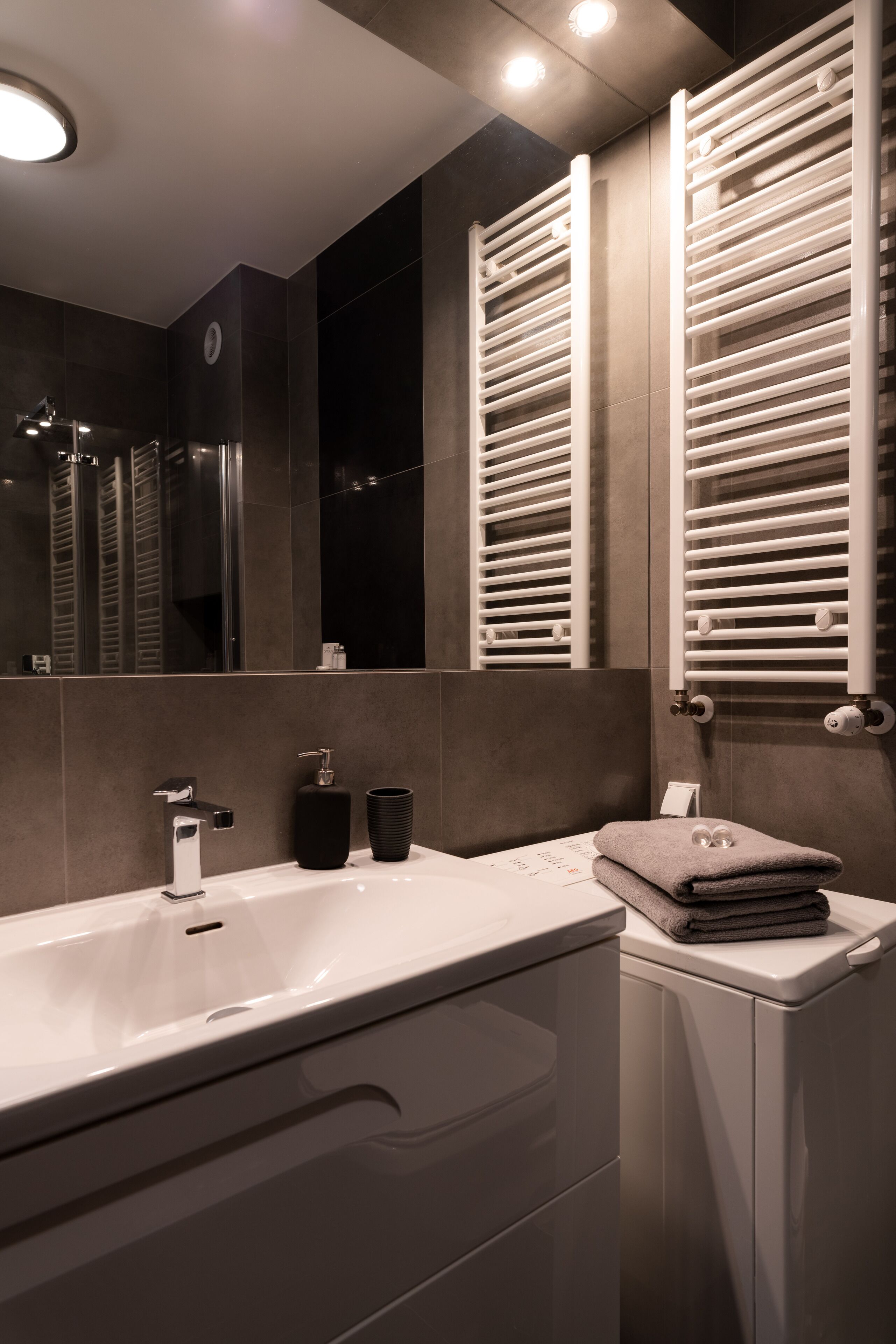 Un baño moderno con un lavamanos blanco, un espejo y un perchero para toallas.