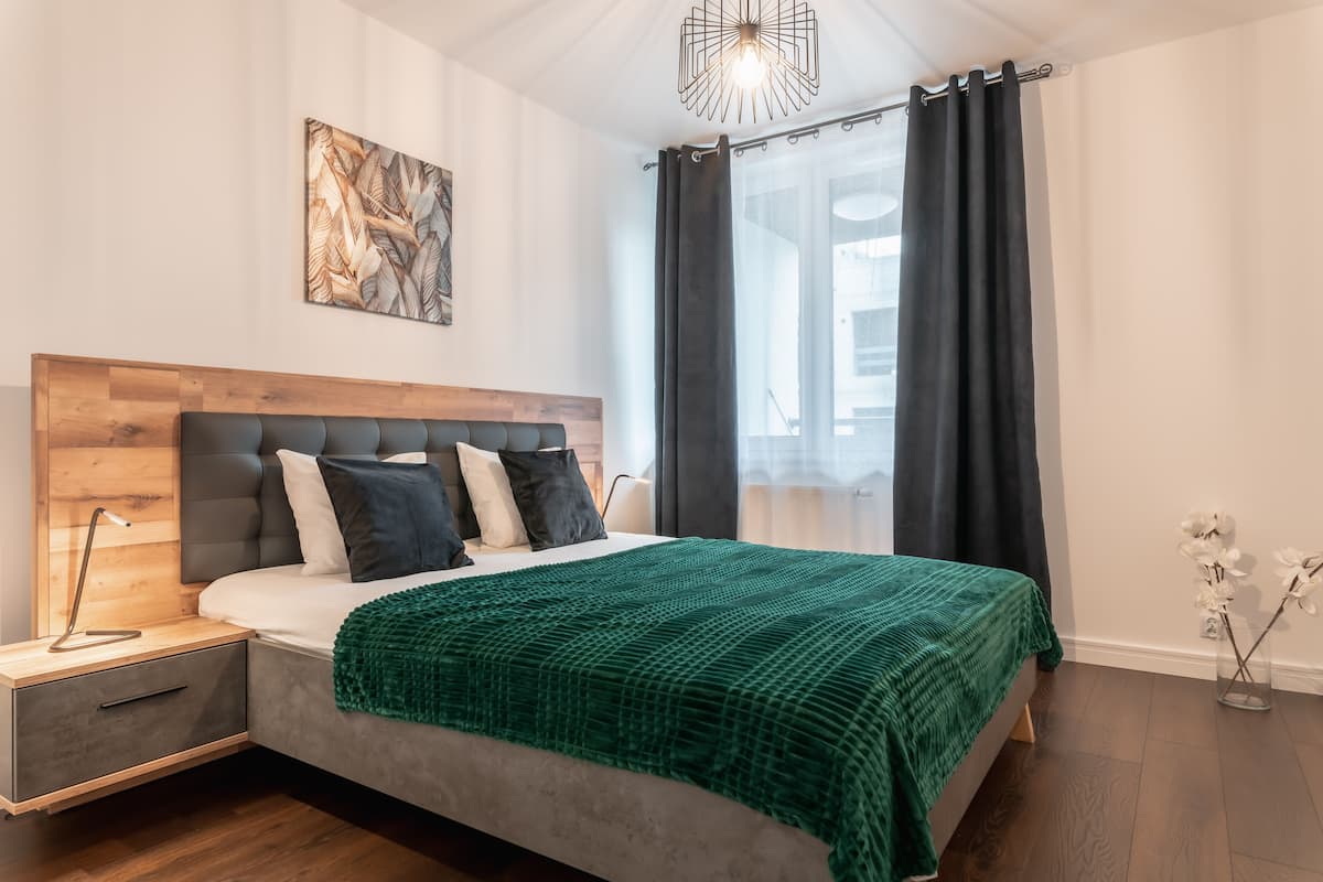 Un dormitorio moderno con cabecera de madera, colcha verde y una mesita de noche con lámpara.