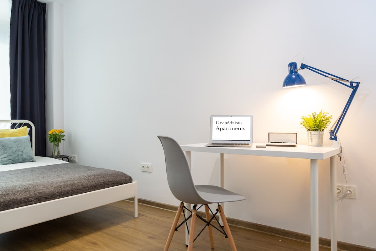 Un dormitorio con una cama, un escritorio con una computadora portátil, una silla, una lámpara y una planta en maceta.