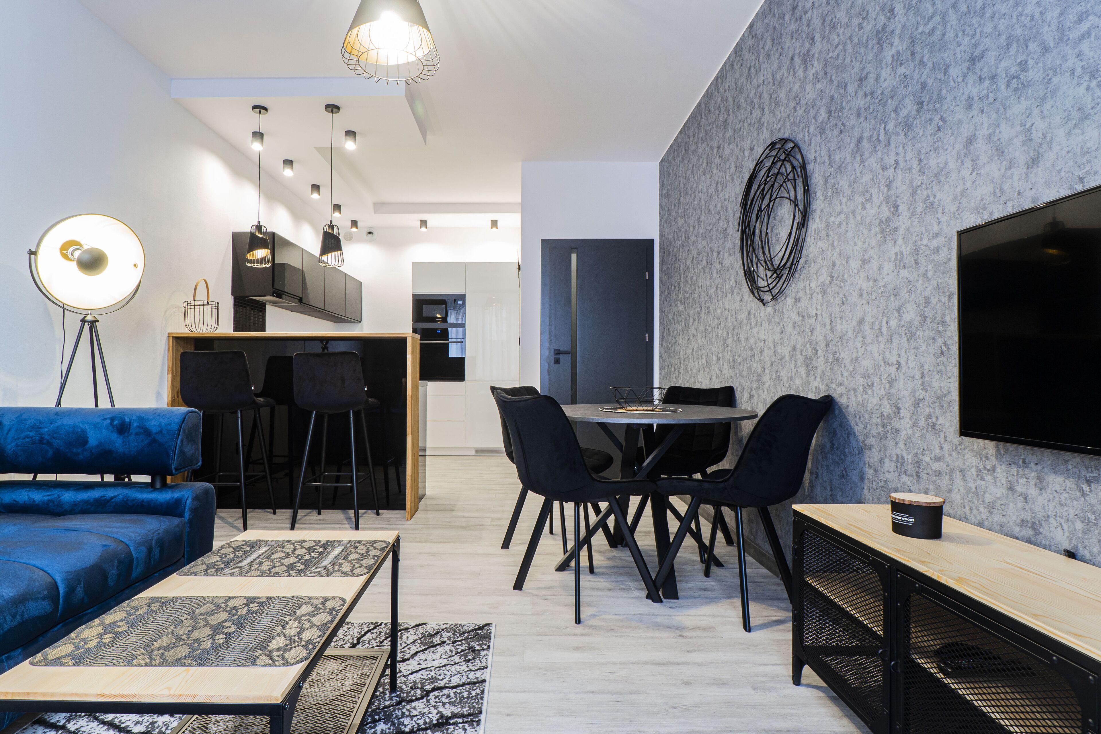 A modern living room with a blue sofa, dining table, and chairs, a coffee table, and a TV on the wall.