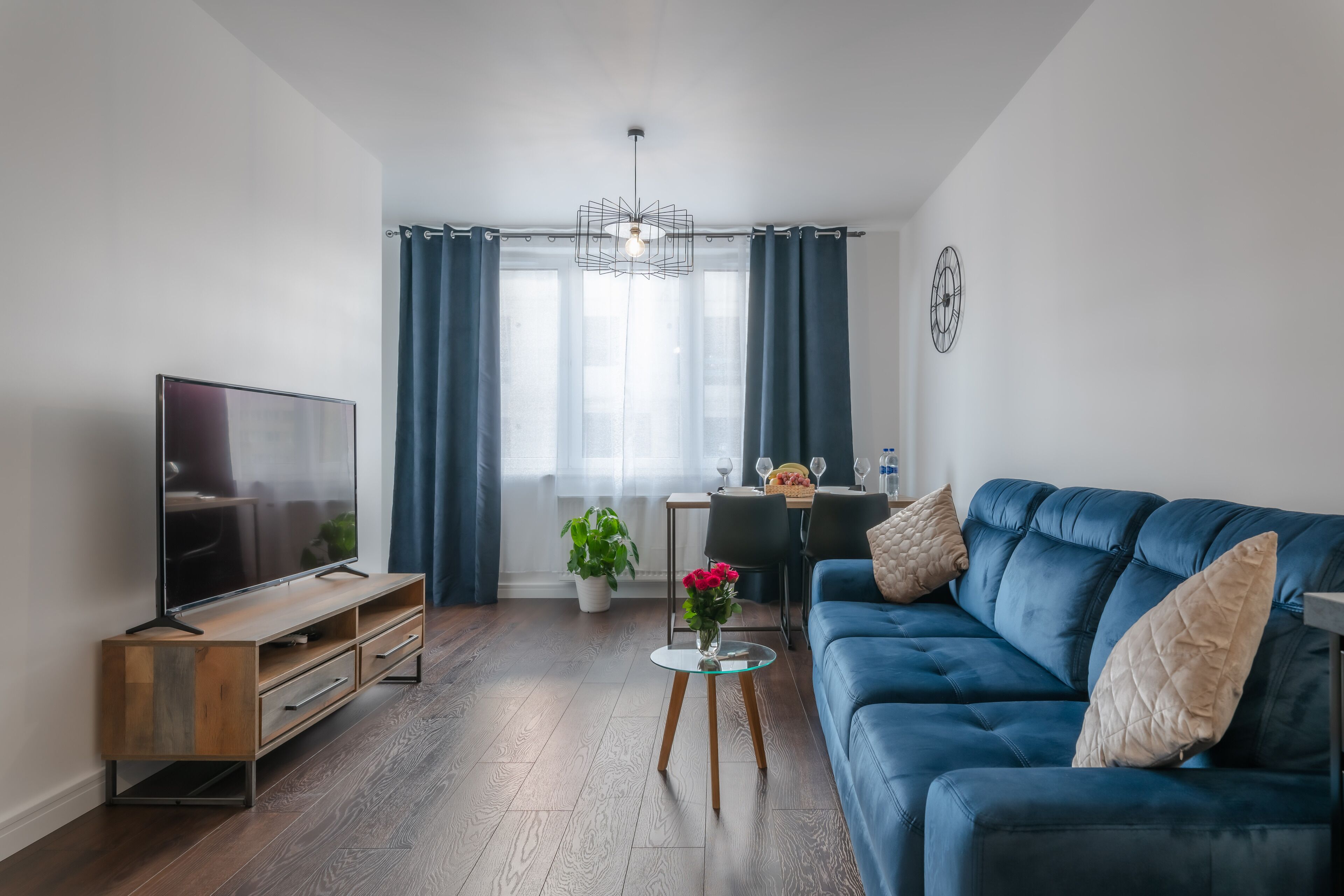Una sala de estar moderna con televisor de pantalla plana, un sofá azul, una mesita de centro y un comedor con mesa y sillas.