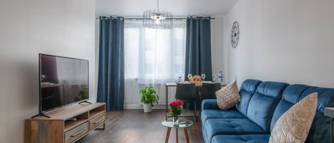 Una sala de estar moderna con televisor de pantalla plana, un sofá azul, una mesita de centro y un comedor con mesa y sillas.