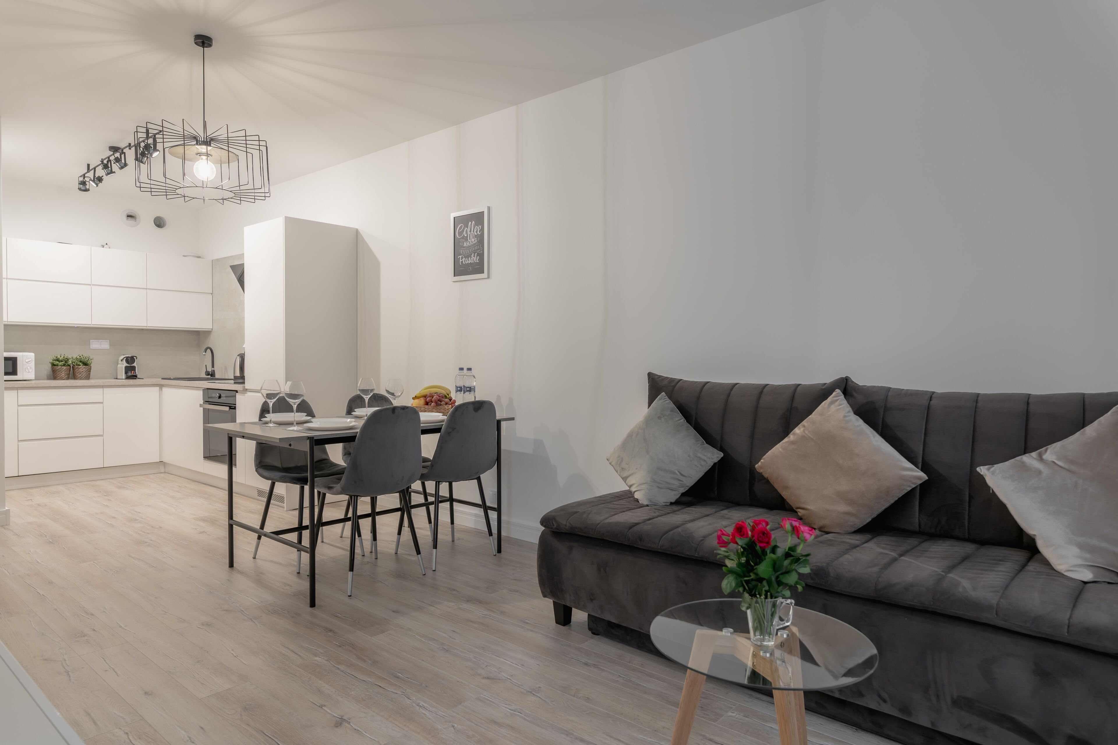 Un salon moderne avec un canapé gris, une table basse en verre et un coin repas comprenant une table et des chaises blanches.