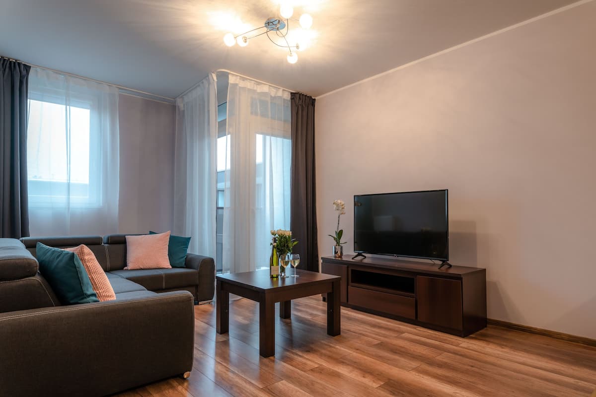Una sala de estar moderna con un sofá, una mesa de centro, un televisor de pantalla plana y un amplio ventanal con cortinas translúcidas.