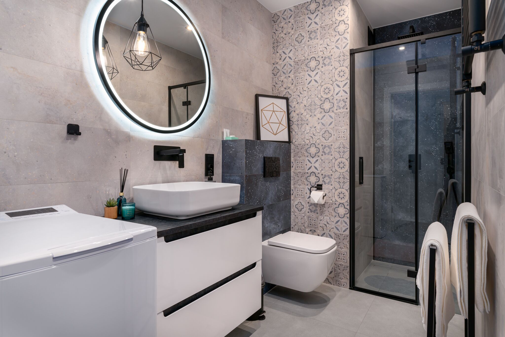 A modern bathroom with a round mirror, a white sink, a toilet, and a glass shower enclosure.