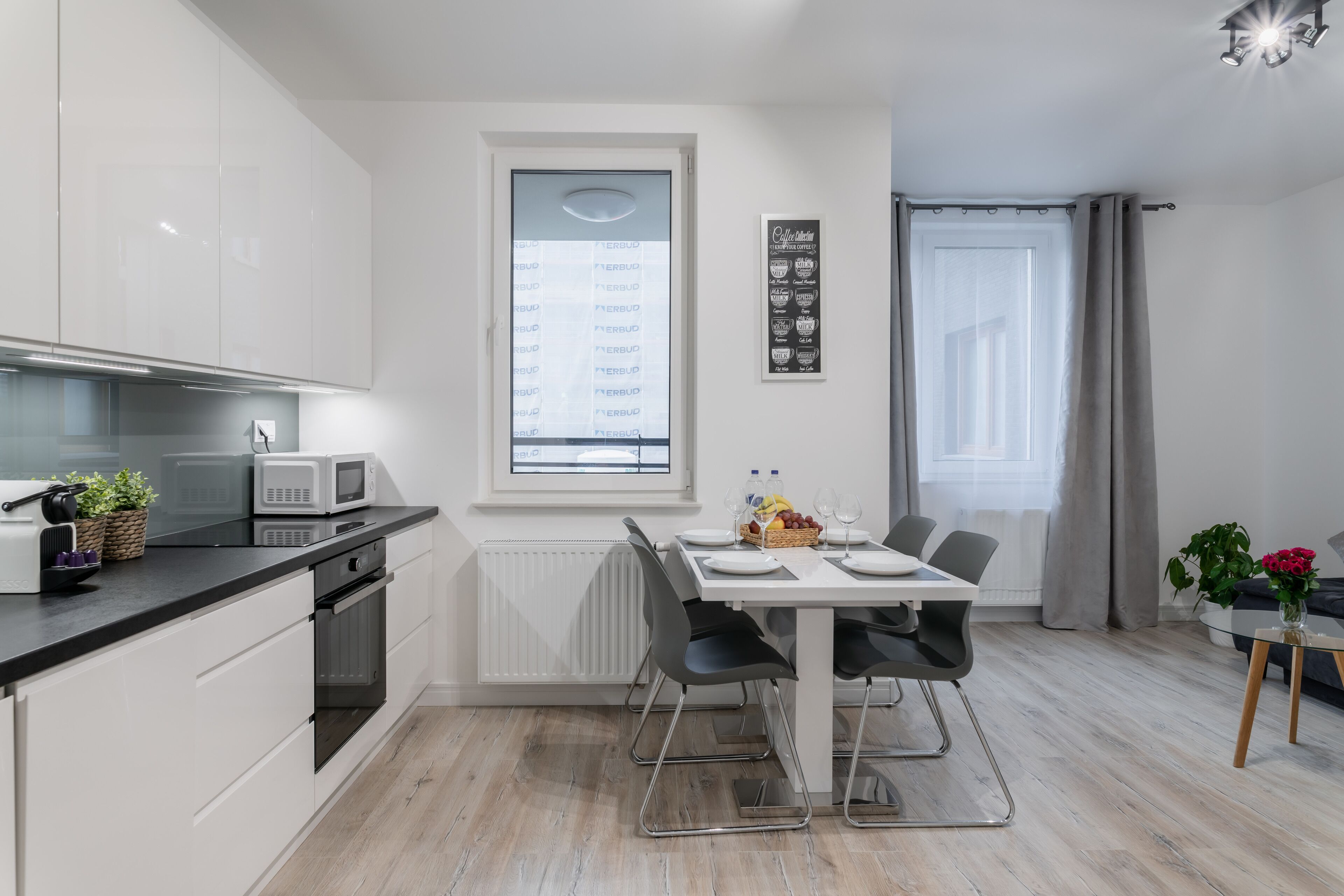 A modern kitchen with white cabinets, a black countertop, and a dining area with a white table and chairs.