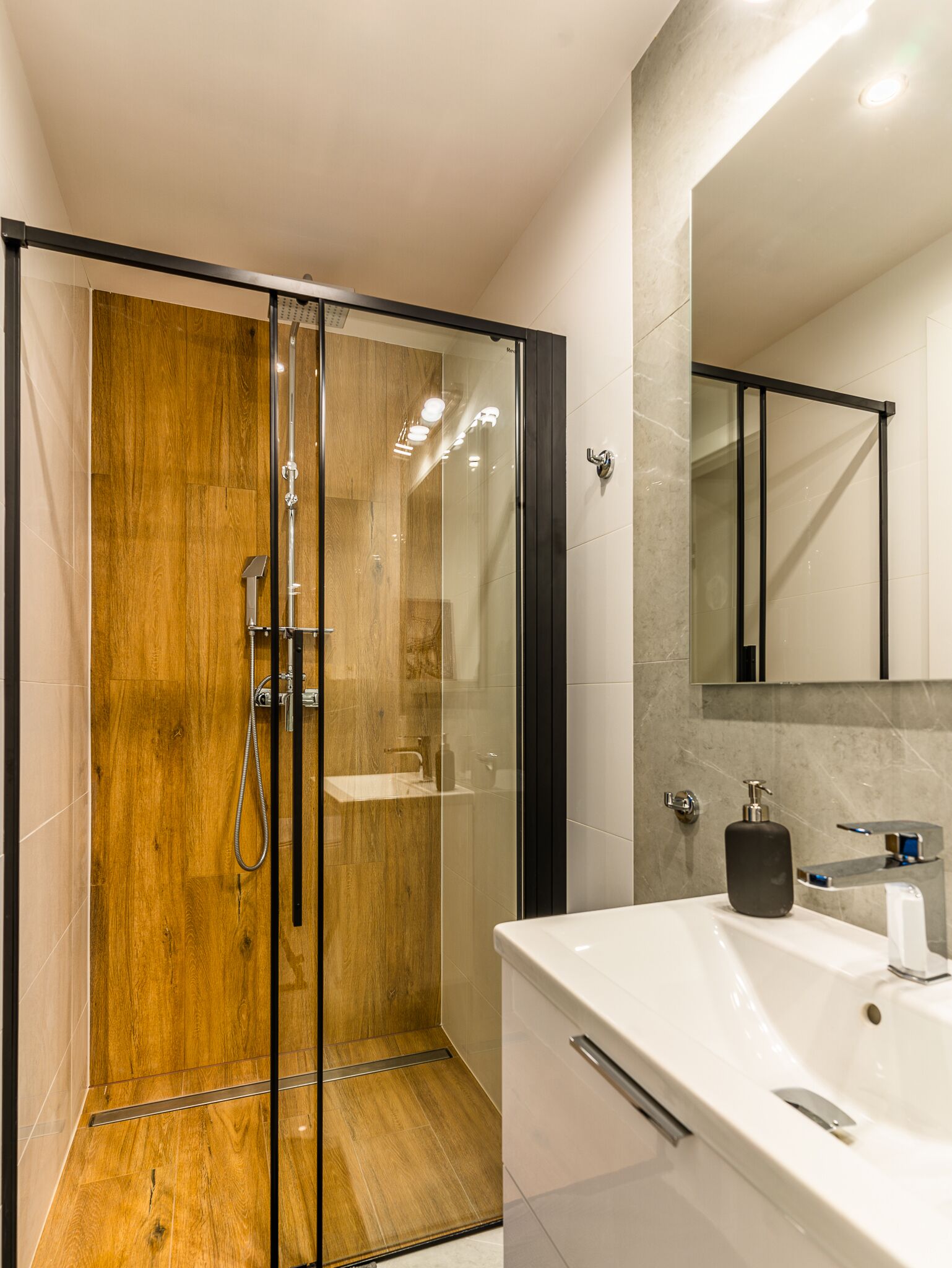 A modern bathroom with a glass-enclosed shower, a white sink, and a marble-tiled wall.