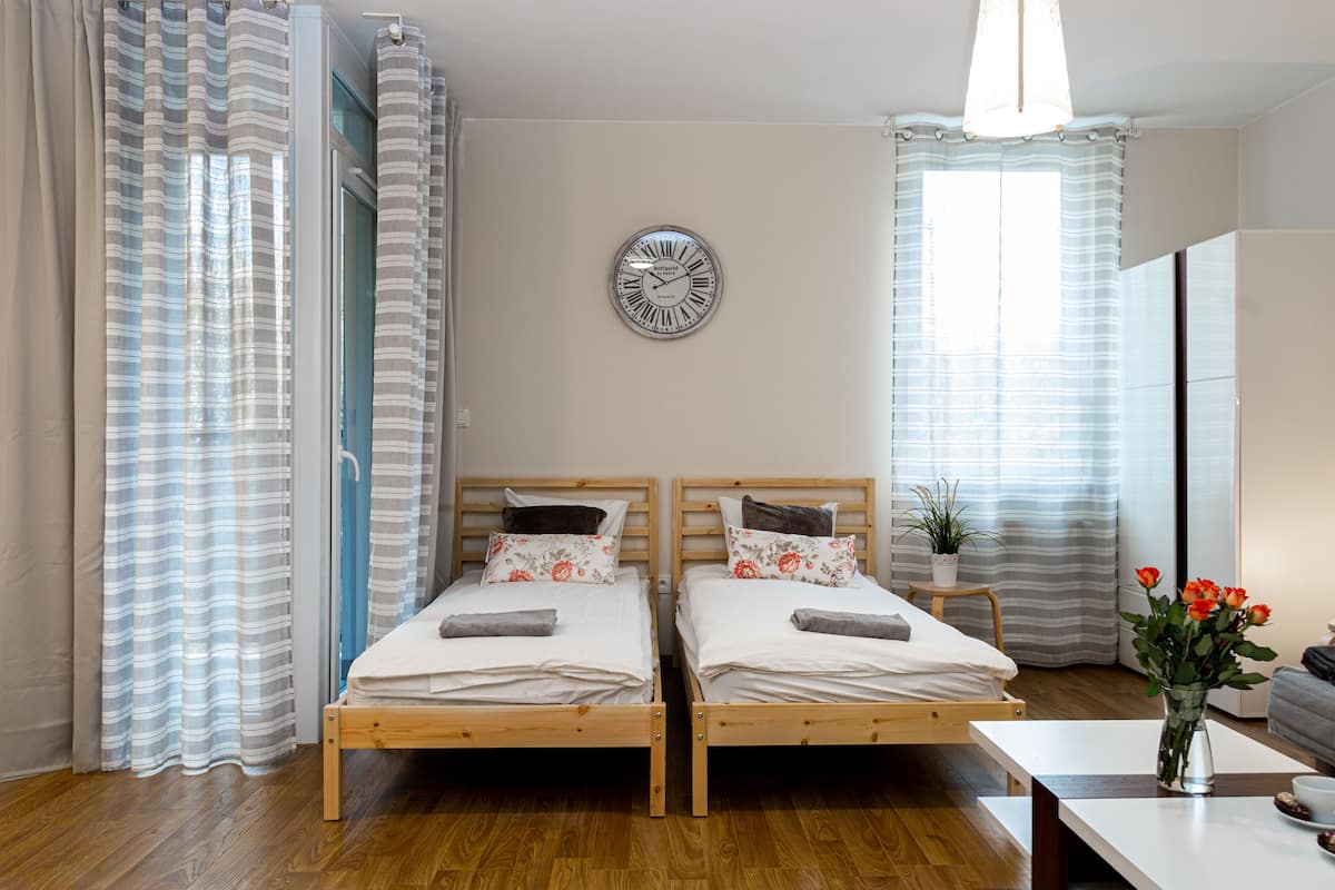 Una habitación con dos camas de madera, un reloj de pared y una ventana con cortinas.