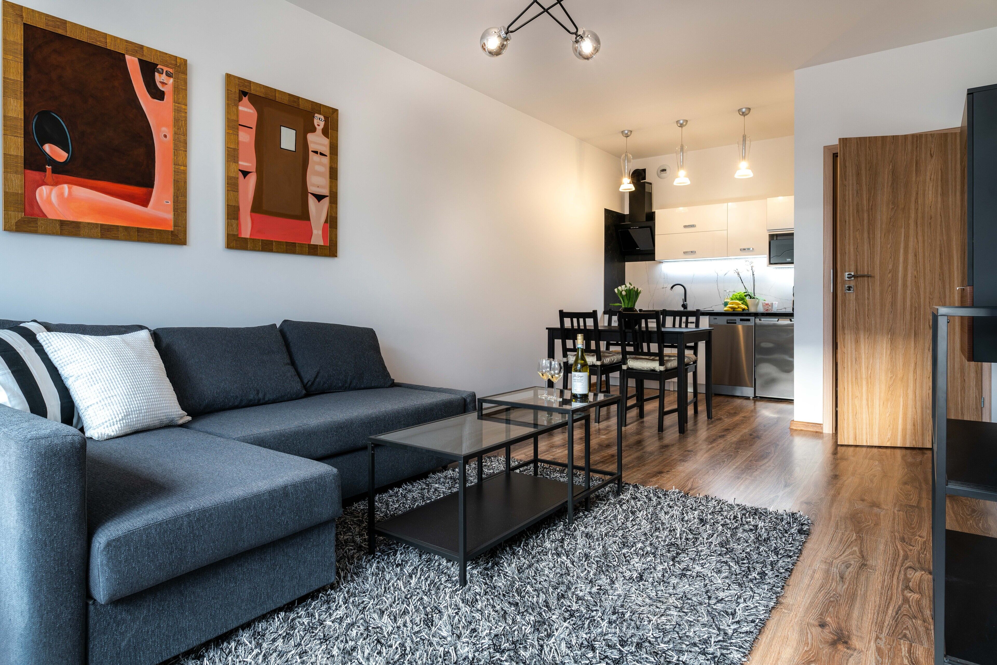 Un salon moderne avec un canapé gris, une table basse en verre et deux tableaux abstraits accrochés au mur.