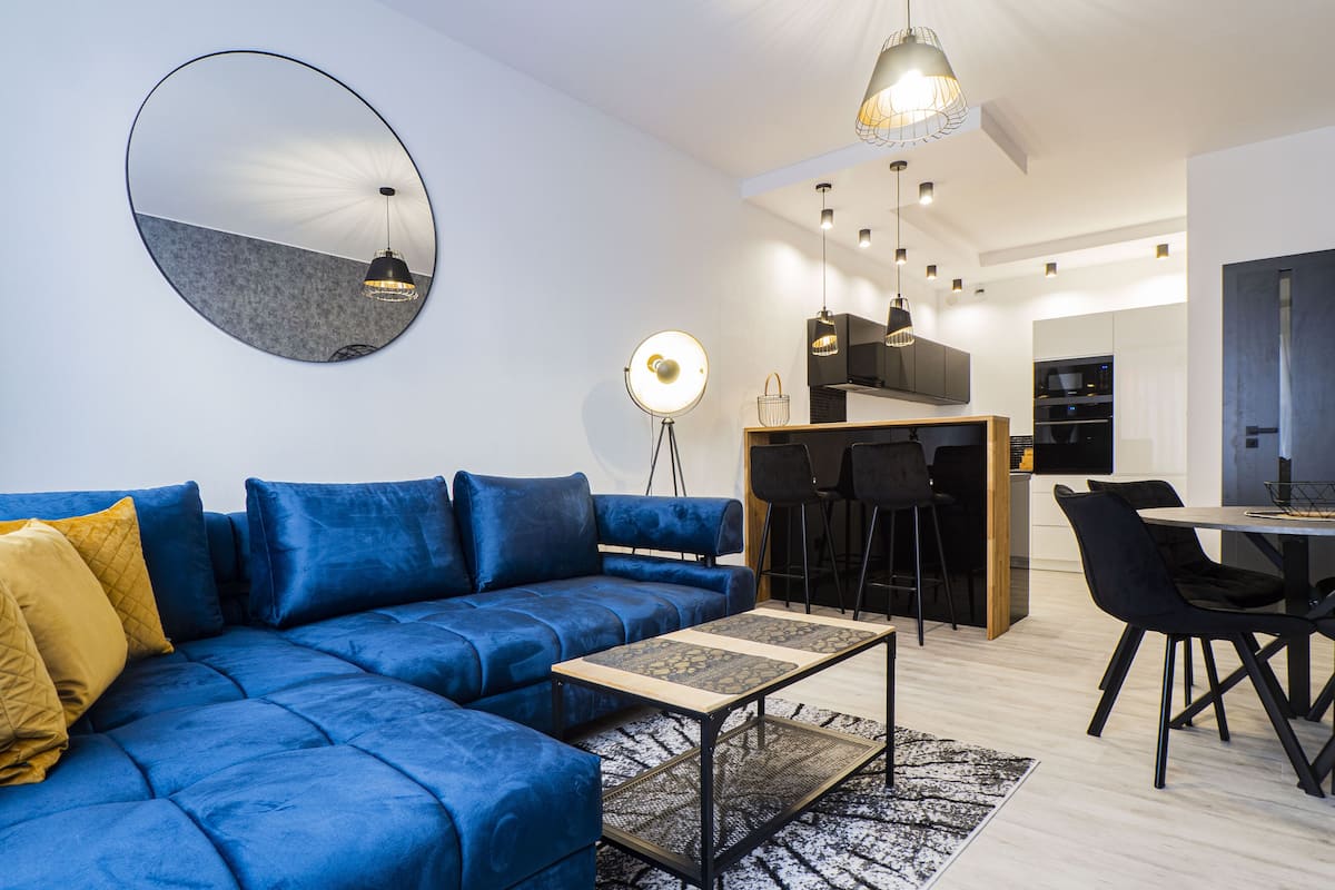 Una sala de estar moderna con un sofá azul, un espejo redondo y un comedor con mesa y sillas.