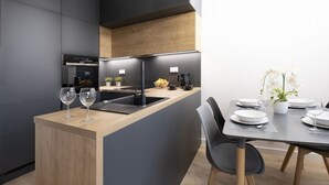 A modern kitchen with dark cabinetry, a wooden island, and a dining area with a table set for two. - Pure Home Apartments - Gwiaździsta (Wroclaw)
