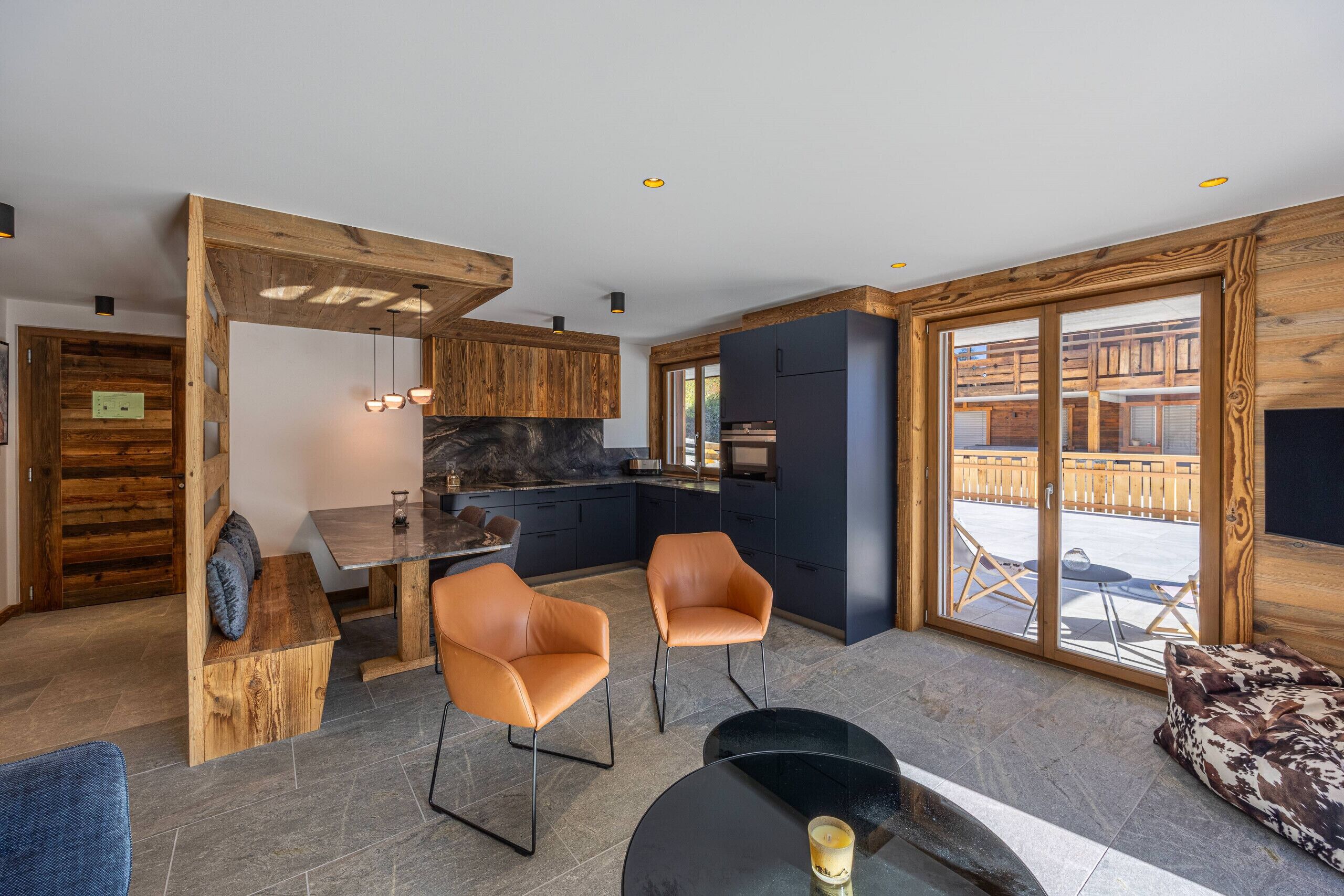 Una cocina moderna con detalles de madera, un área de comedor con sillas de cuero y un amplio ventanal corredera a un patio exterior.