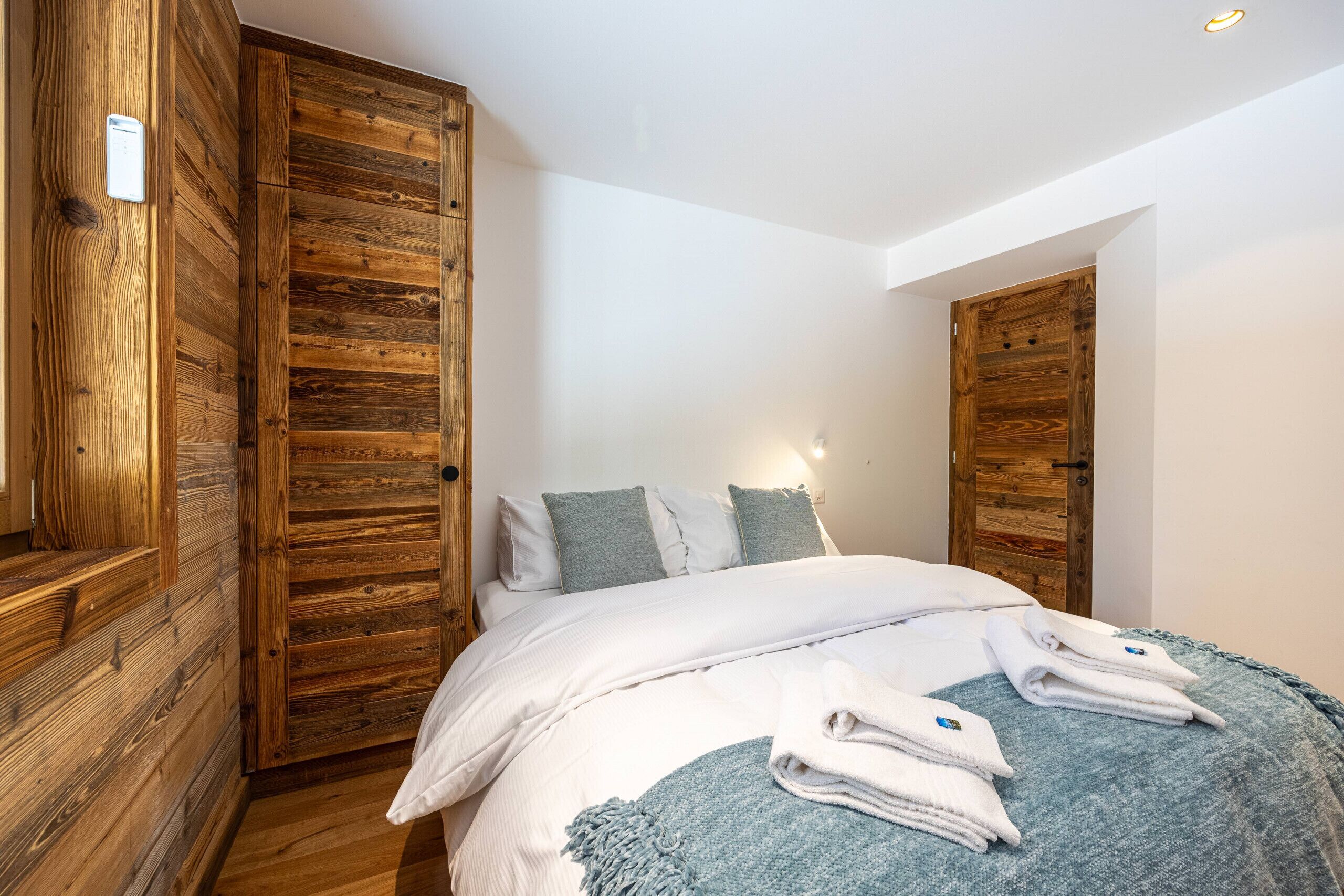 A bedroom with a wooden wardrobe, a bed with white bedding, and a blue throw blanket.