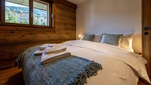 Ein Schlafzimmer mit Holzboden, einem großen Fenster, einem Bett mit weißen Leinen und einer blauen Zudecke.