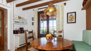Una mesa de comedor de madera con sillas, un frutero y un colgador de luces en una habitación con vigas de madera, una ventana y un sofá verde.