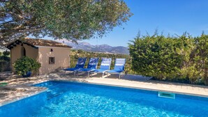 Una piscina con azulejos azules, rodeada de sillas de descanso y un pequeño edificio con techo de tejas.