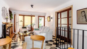 A living room with a checkered floor, white sofas, a wooden chair, a glass table, and a fireplace. - Cas Pedri (Can Picafort)