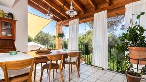 A wooden balcony with a table and chairs, a hanging plant, and a view of greenery. - Cas Pedri (Can Picafort)