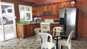 Une cuisine avec des meubles en bois, un réfrigérateur en acier inoxydable, une table en verre avec des chaises et un sol imitant la pierre.