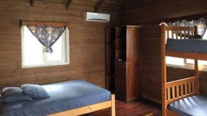 Une chambre dans un chalet en bois, équipée d’un lit superposé, d’un lit simple, d’une fenêtre avec des rideaux et d’un appareil de climatisation.