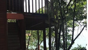 Une structure en bois dotée d’un balcon donnant sur une étendue d’eau, le tout entouré d’arbres.