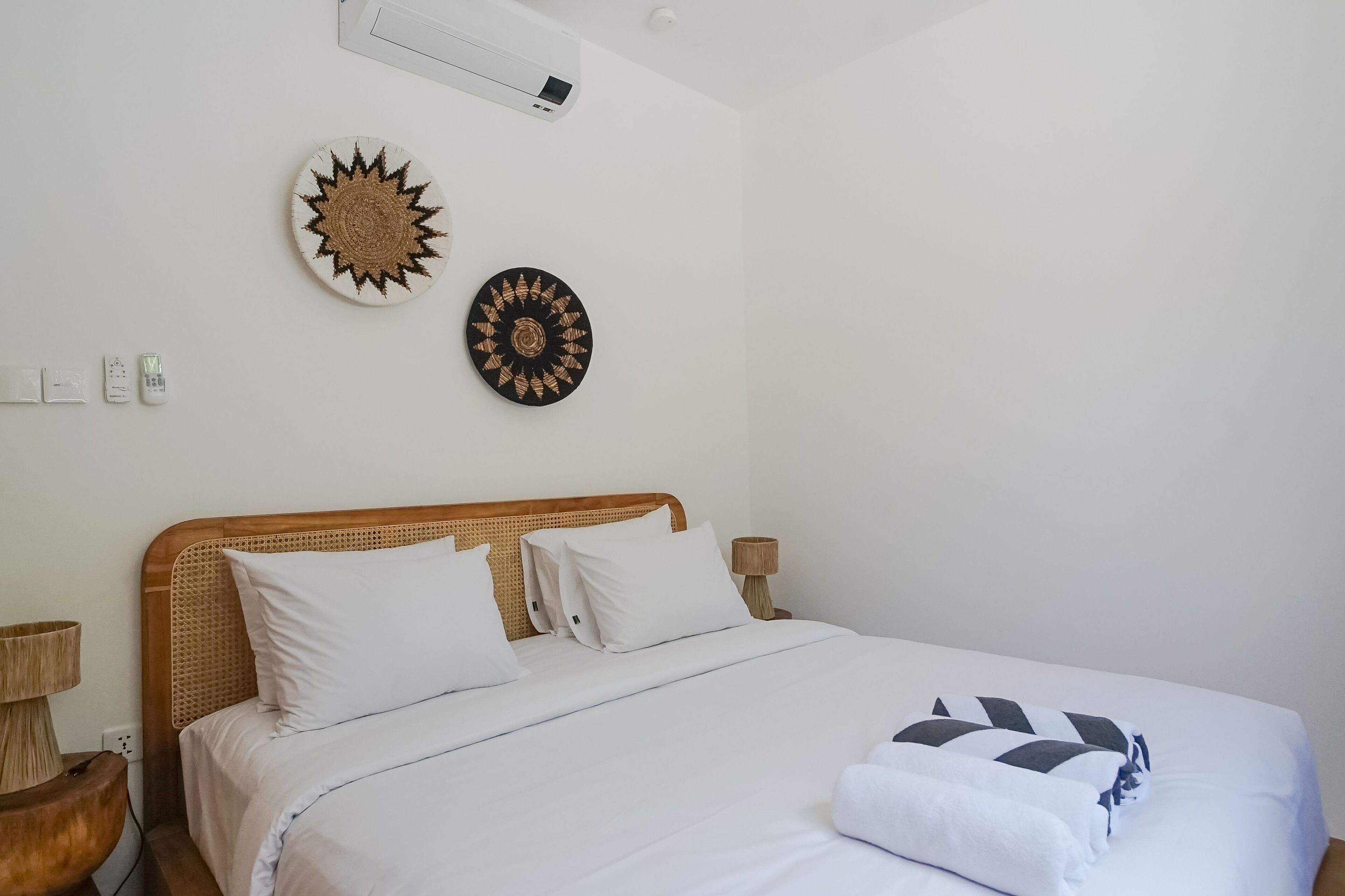 A neatly made bed with white linens, a wooden headboard, and two wall-mounted decorative plates.
