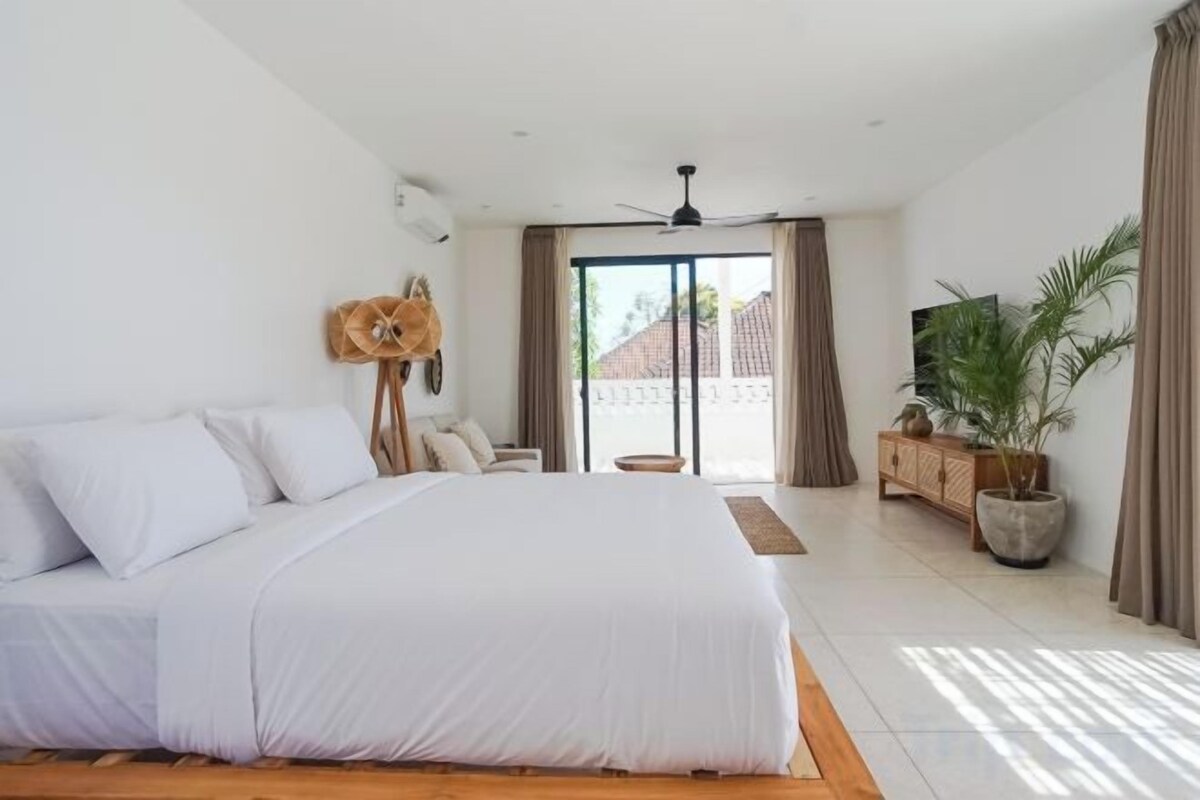 Un dormitorio con una cama grande, ventilador de techo, televisor y vistas al exterior.