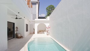 A modern pool area with a clear pool, white walls, and a ceiling fan. - Avanoa Villa (Canggu)