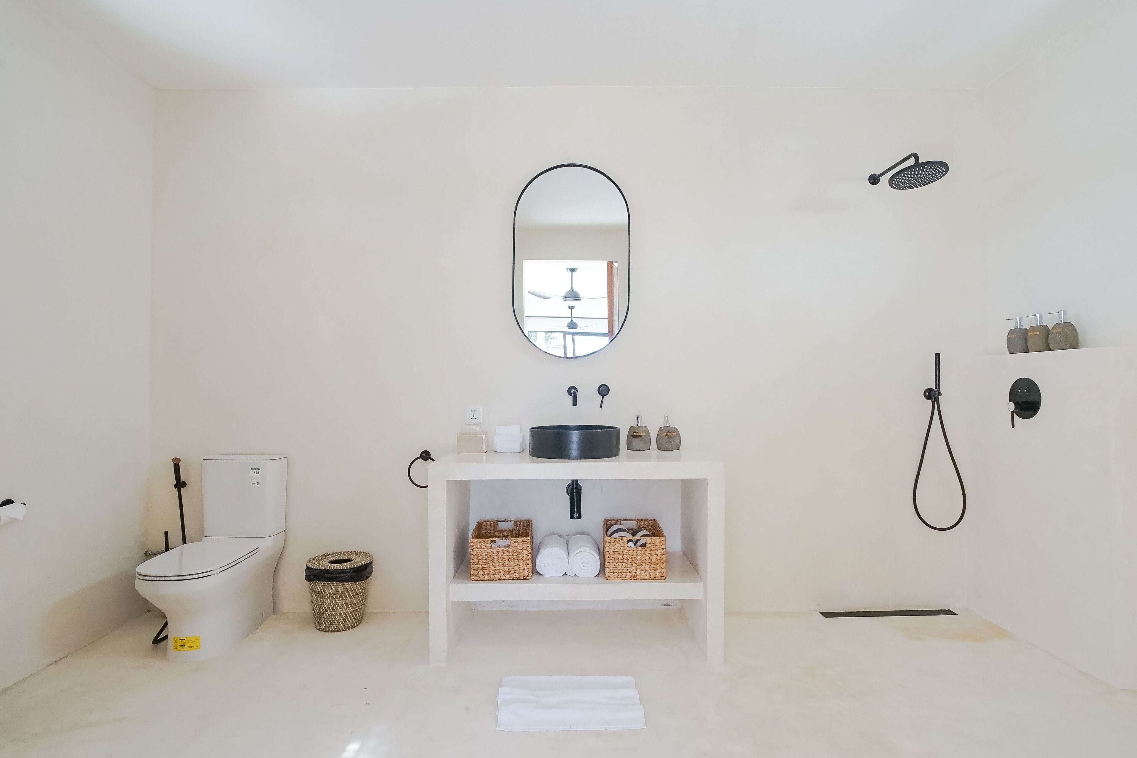 A bathroom with a toilet, sink, mirror, shower, and storage shelves.