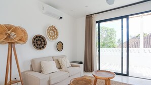 A modern living room with a sofa, a standing fan, and decorative wall art. - Avanoa Villa (Canggu)