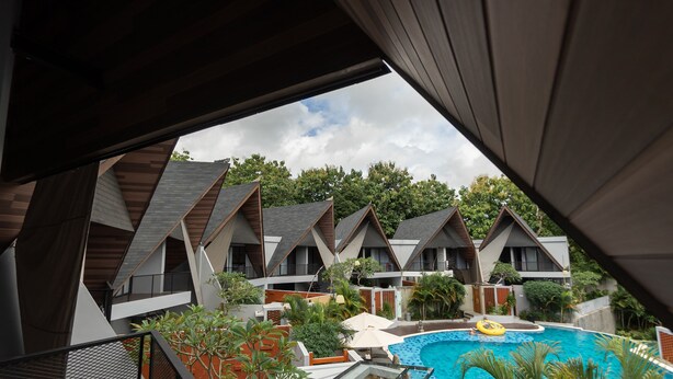 A view of a hotel with multiple bungalow-style rooms, a swimming pool, and surrounding greenery. - The Dan-els By Zuzu (Nusa Dua)