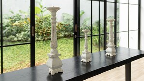 A black table with three white candle holders against a window with black frames. - The Dan-els By Zuzu (Nusa Dua)