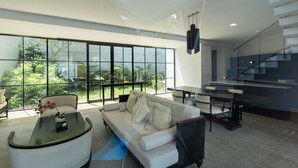 A modern living room with a sofa, coffee table, and dining area. - The Dan-els By Zuzu (Nusa Dua)
