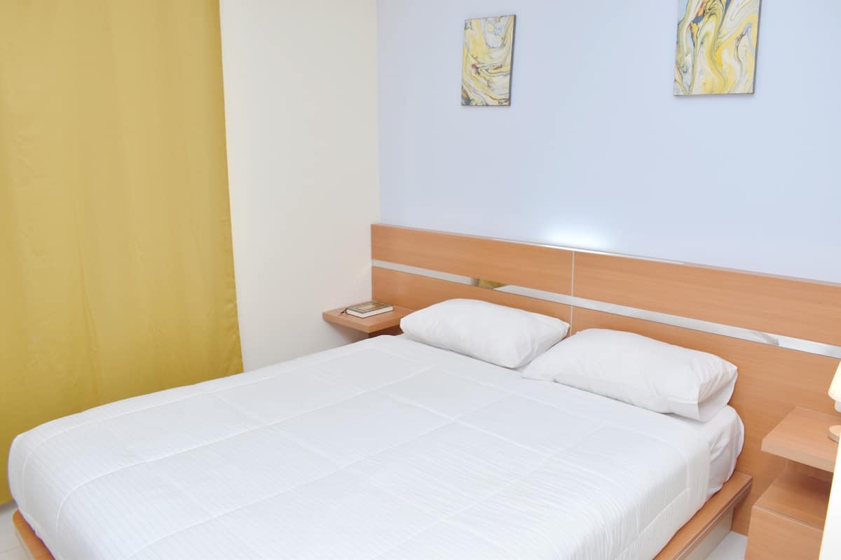 A neatly made bed with white linens, a wooden headboard, and a bedside table with a lamp.