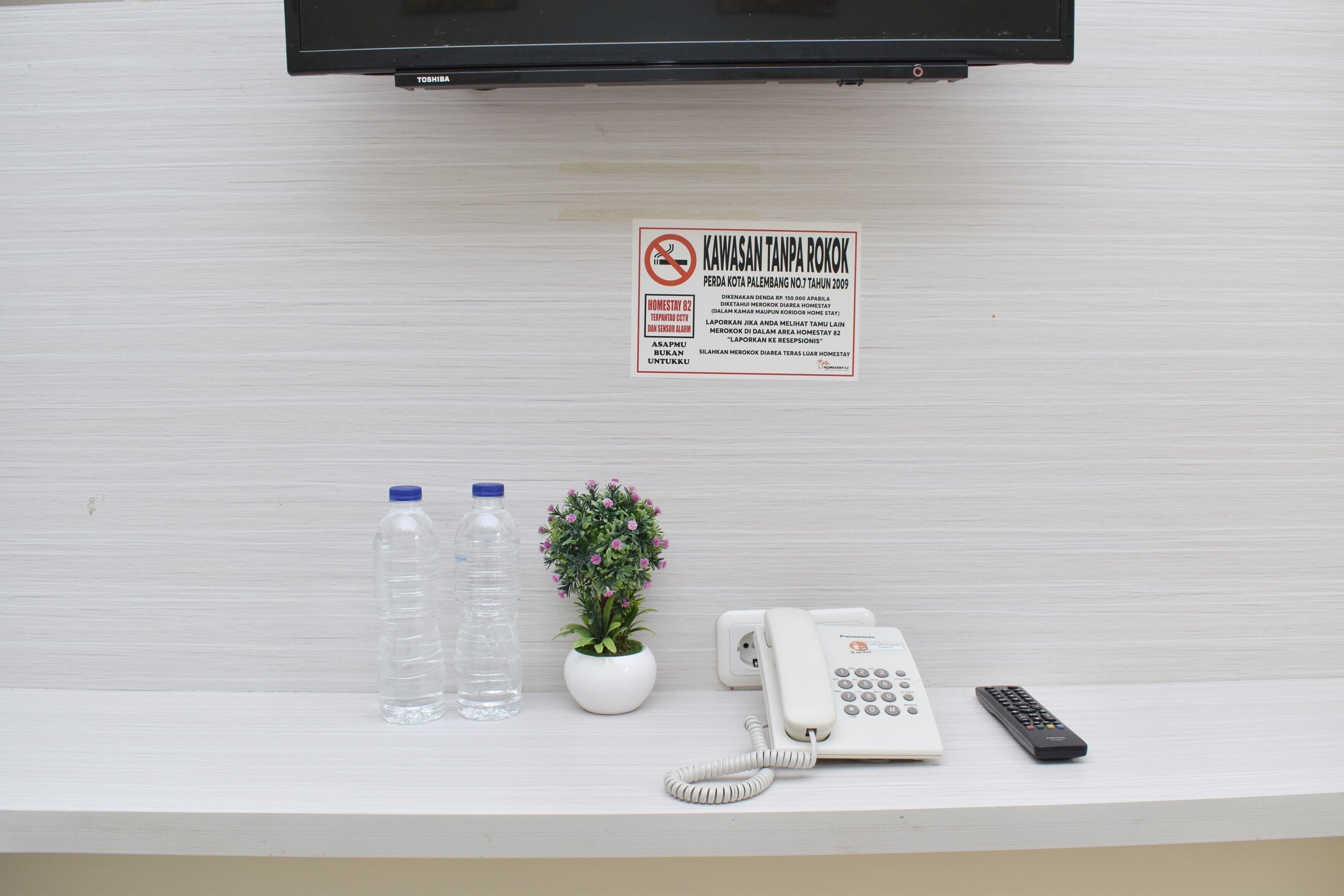 A reception desk with a sign, a water bottle, a potted plant, a telephone, and a remote control.