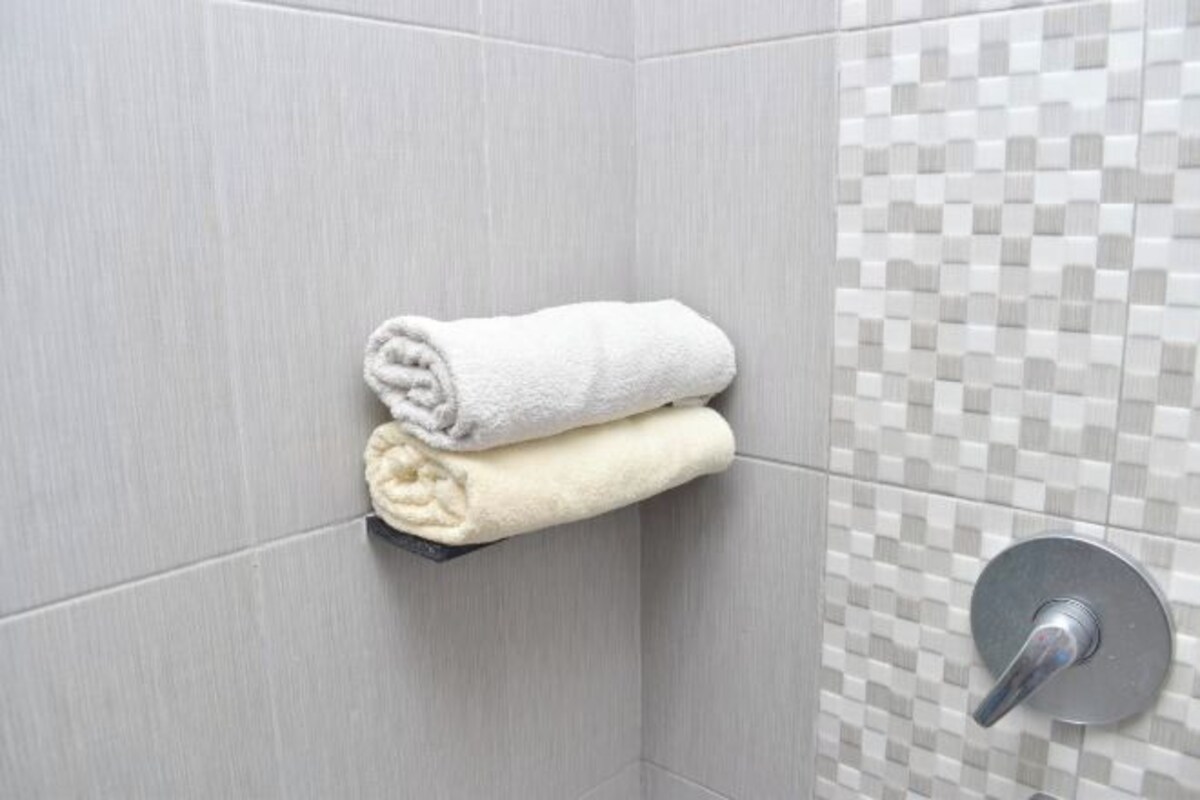 A bathroom with grey tiled walls, a towel rack holding two towels, and a shower control panel.