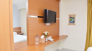 A hotel room with a wooden reception desk, a flat-screen TV mounted on the wall, a bedside table with a lamp, a telephone, and a small decorative item. - Homestay 82 Syariah Palembang (Palembang)