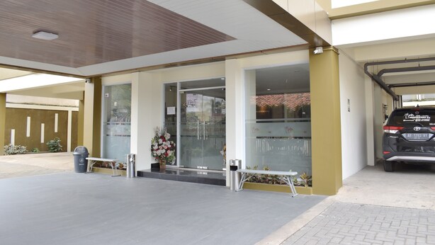 A building entrance with a glass door, a bench, a trash bin, and a Toyota SUV parked inside. - Homestay 82 Syariah Palembang (Palembang)