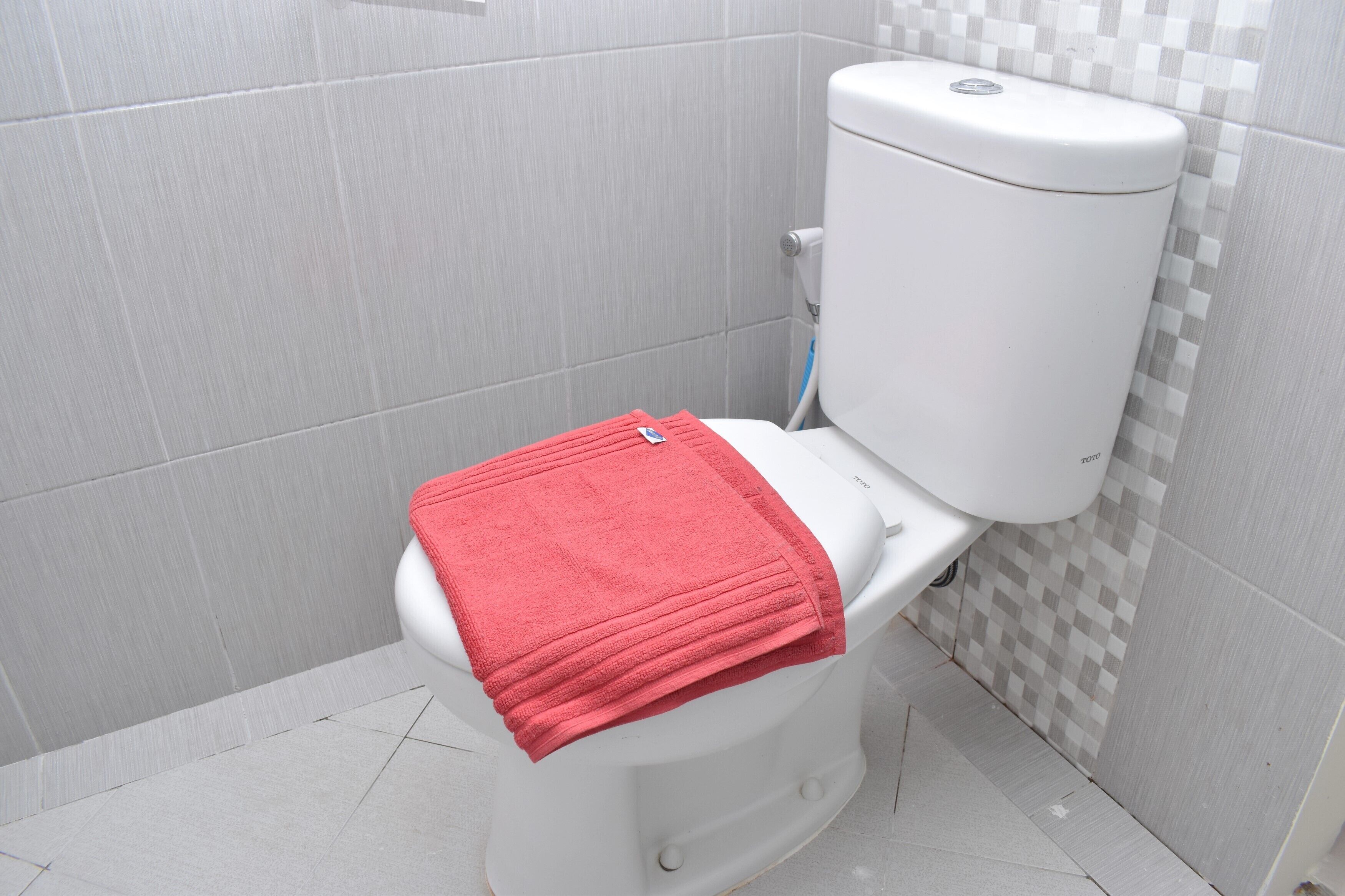A white toilet with a red towel on the seat and a checkered tile wall behind it.