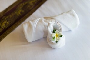 Une serviette blanche, soigneusement pliée, ornée d’une fleur blanche, posée sur une surface blanche.