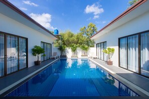 Une piscine intérieure moderne, avec une eau d’un bleu cristallin, entourée de murs blancs et de grandes fenêtres.