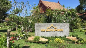 Señal de The Casita Phuket con un techo tradicional tailandés, rodeado de exuberante vegetación y plantas en flor.