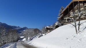 Une route de montagne enneigée, avec un bâtiment en bois sur la droite.