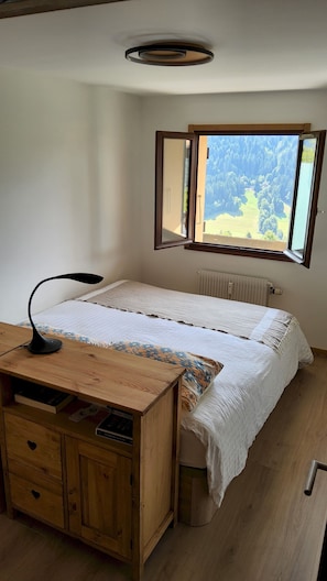 Un dormitorio con cama, escritorio de madera, lámpara y ventana con vistas a un bosque.